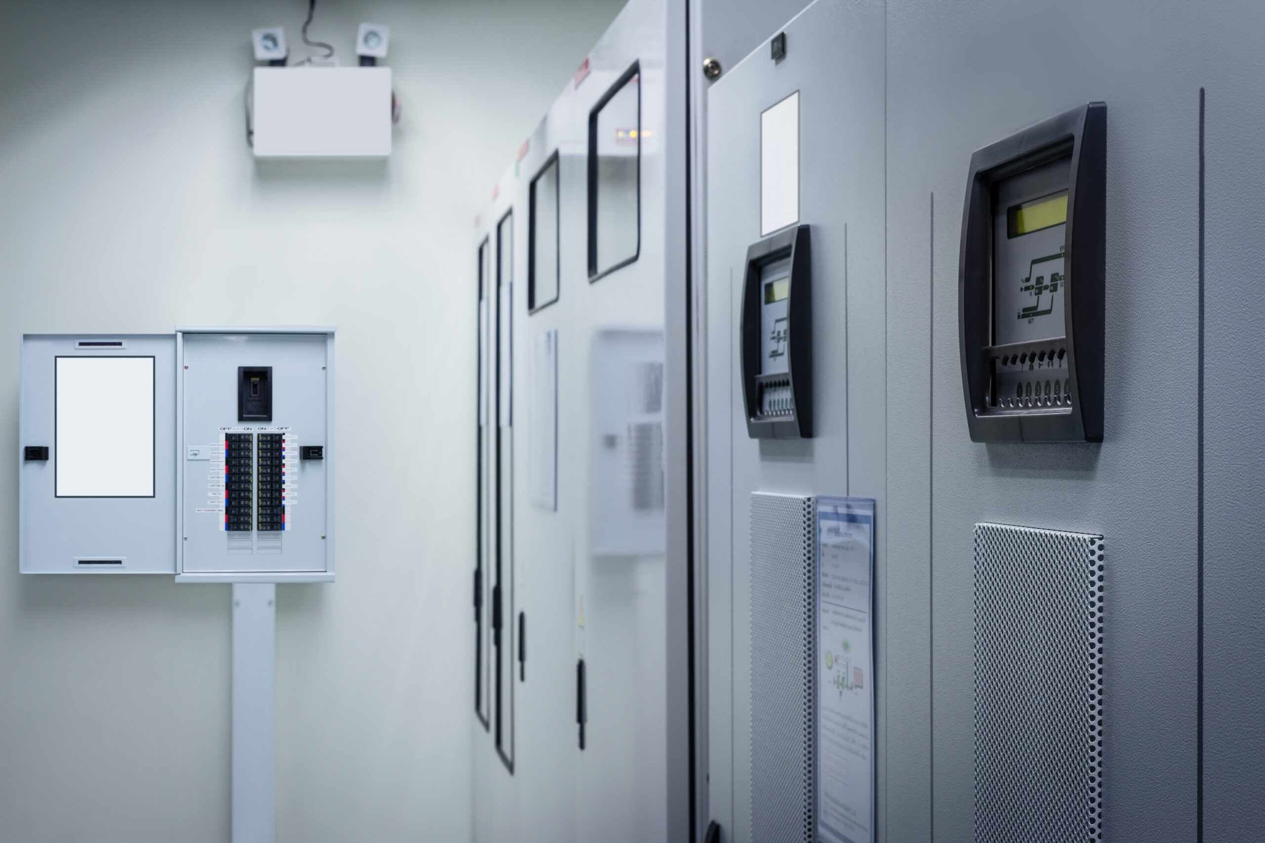 Interior of a data centre panel room with multiple control panels and circuit breakers on a clean white wall. - CSA Catapult