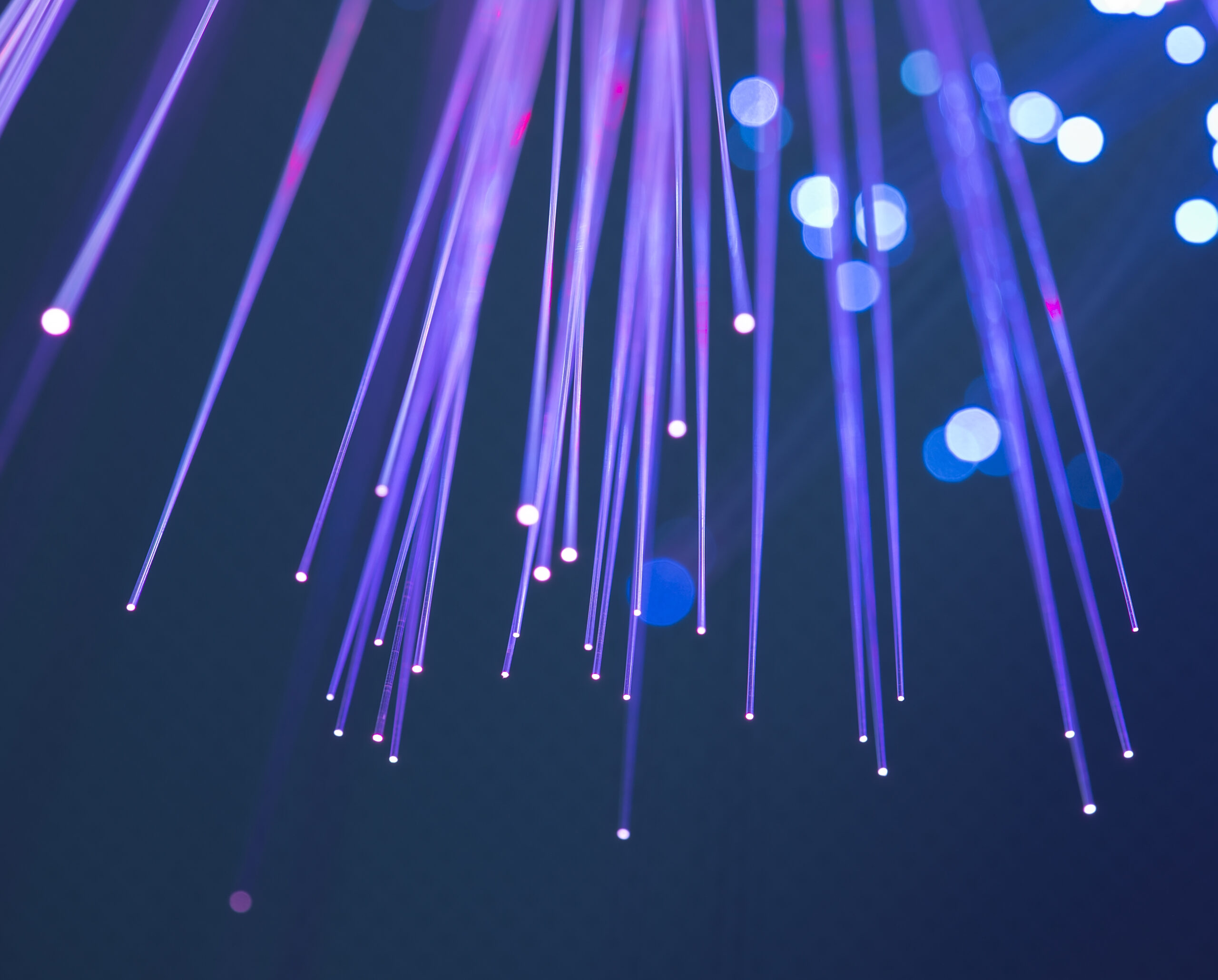 Close-up of glowing fiber optic strands in blue and purple hues, with circular light bokeh in the background. - CSA Catapult