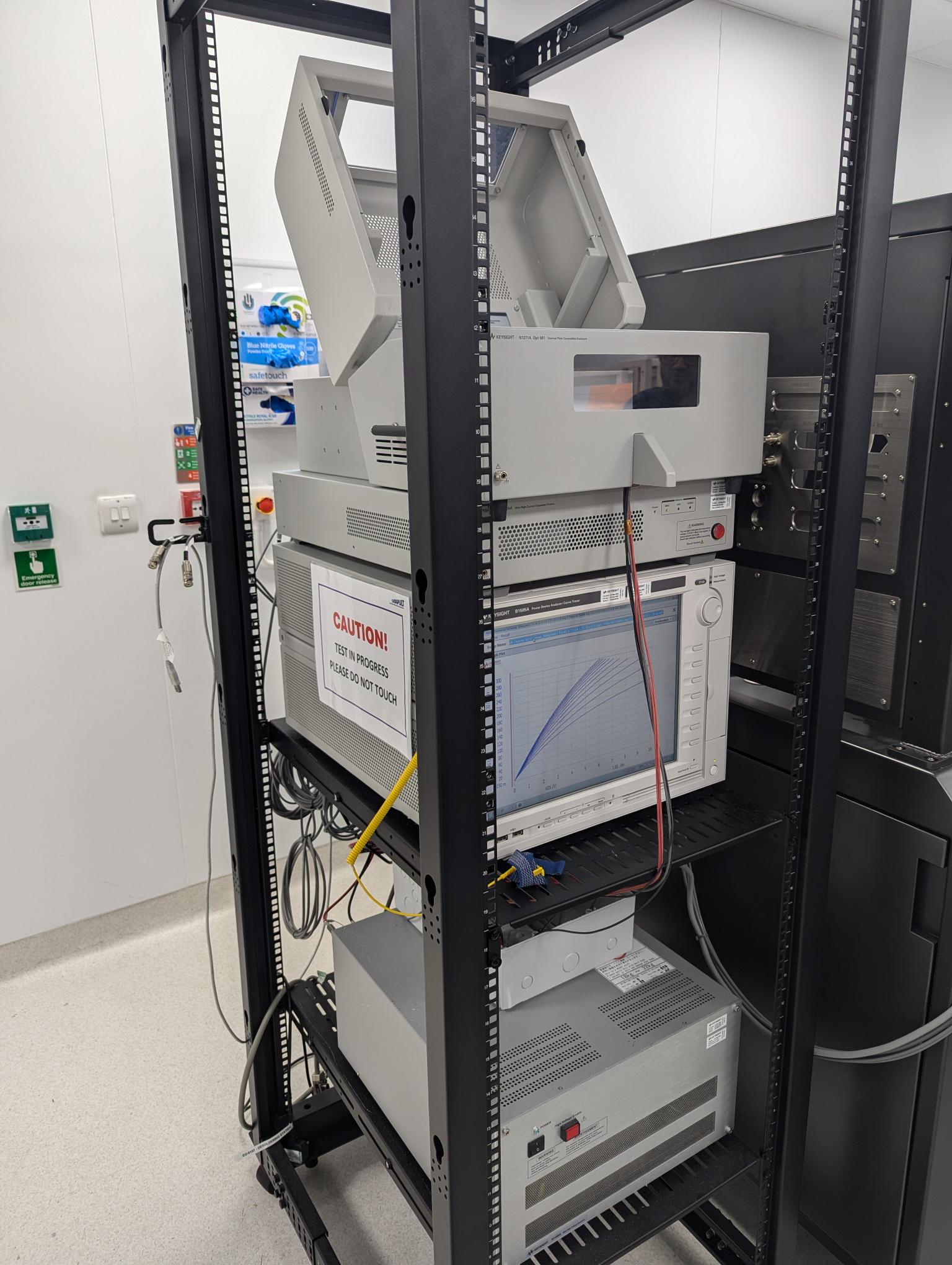 A rack with the Keysight B1505 Power Device Analyzer and cables; a caution sign is displayed on one unit. - CSA Catapult