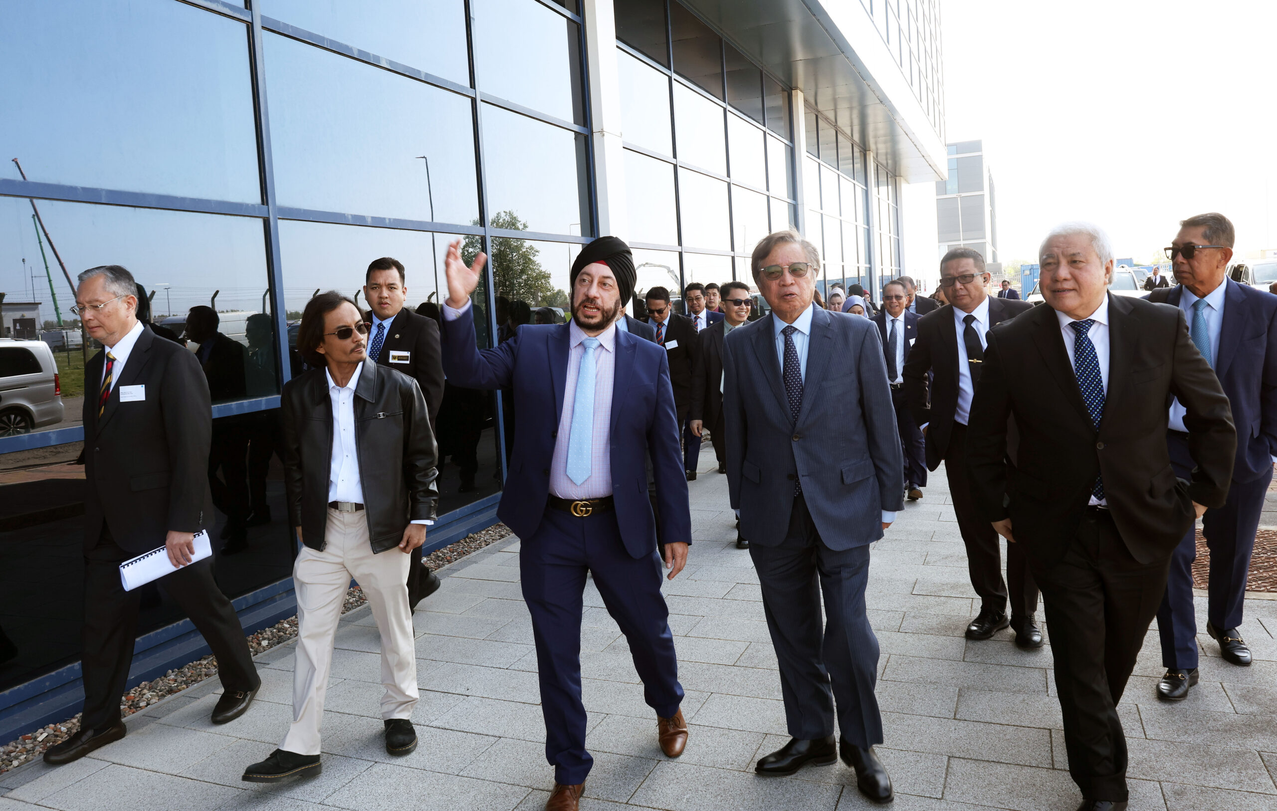 A group of businesspeople in suits walk together outside a modern glass building in Sarawak. - CSA Catapult