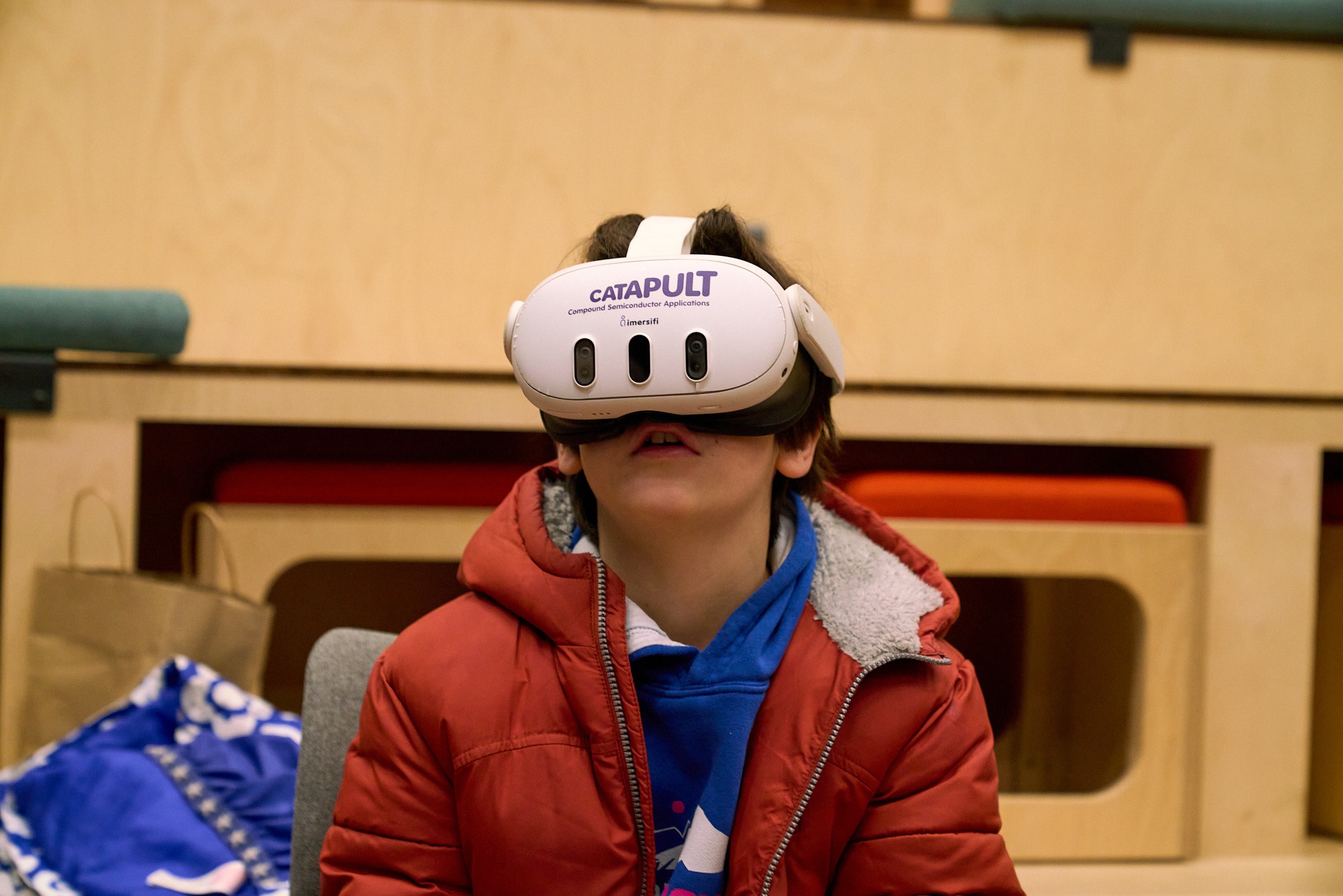 A child in a red jacket uses a white VR headset labeled 