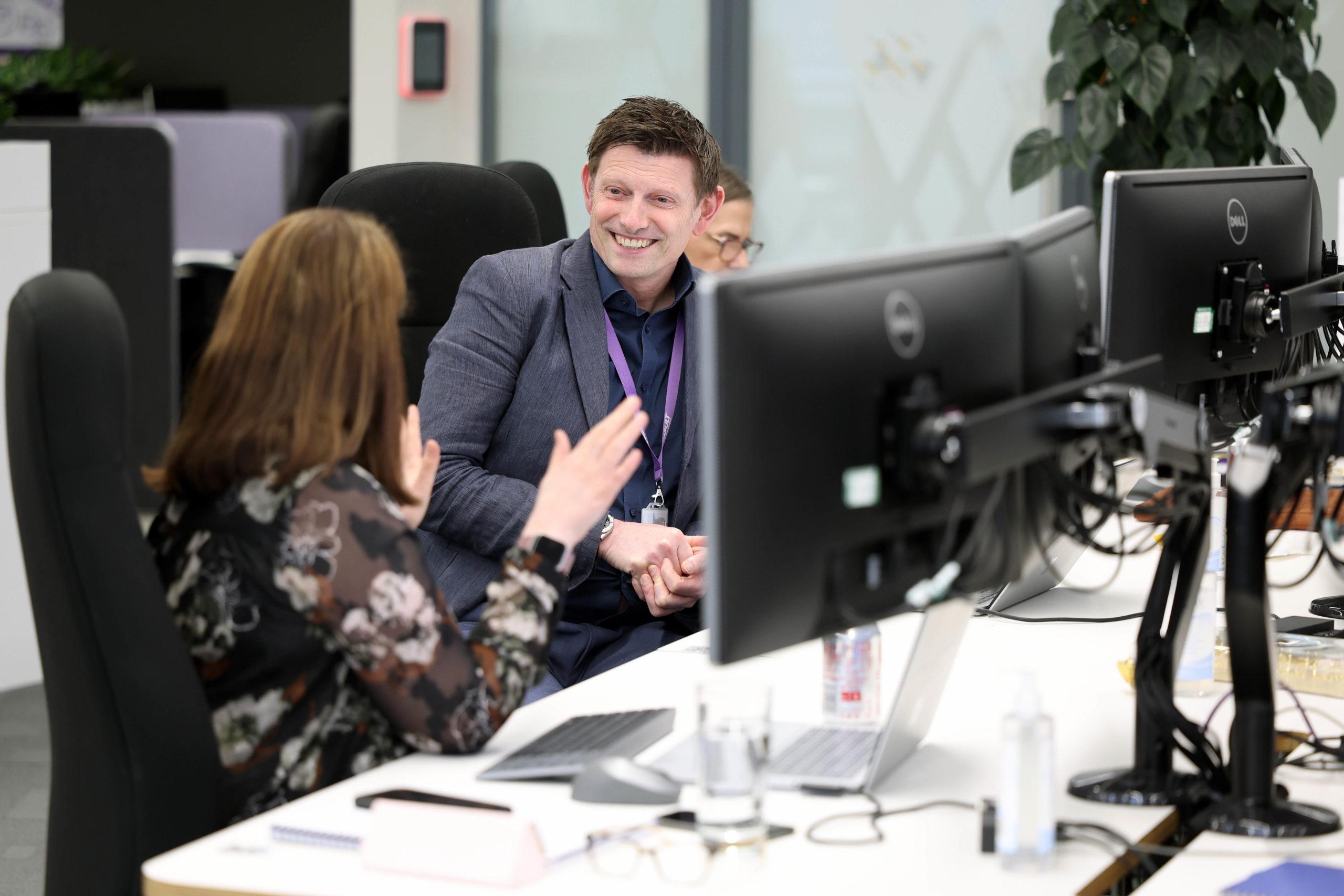 Two people sit at desks with computer monitors, talking and smiling in a modern office environment. - CSA Catapult