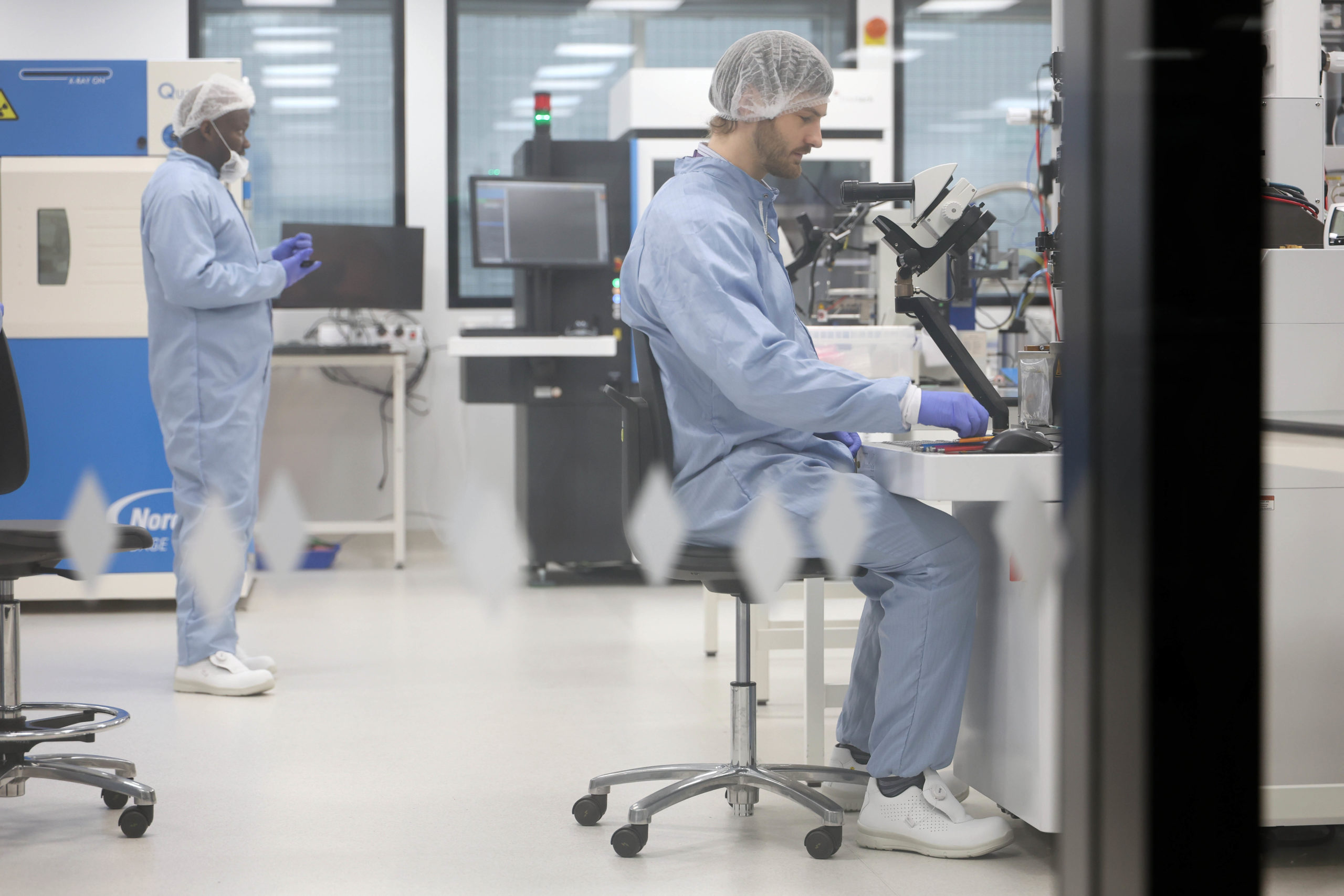 Two scientists in lab coats and hairnets work in a modern laboratory with equipment and computers. - CSA Catapult