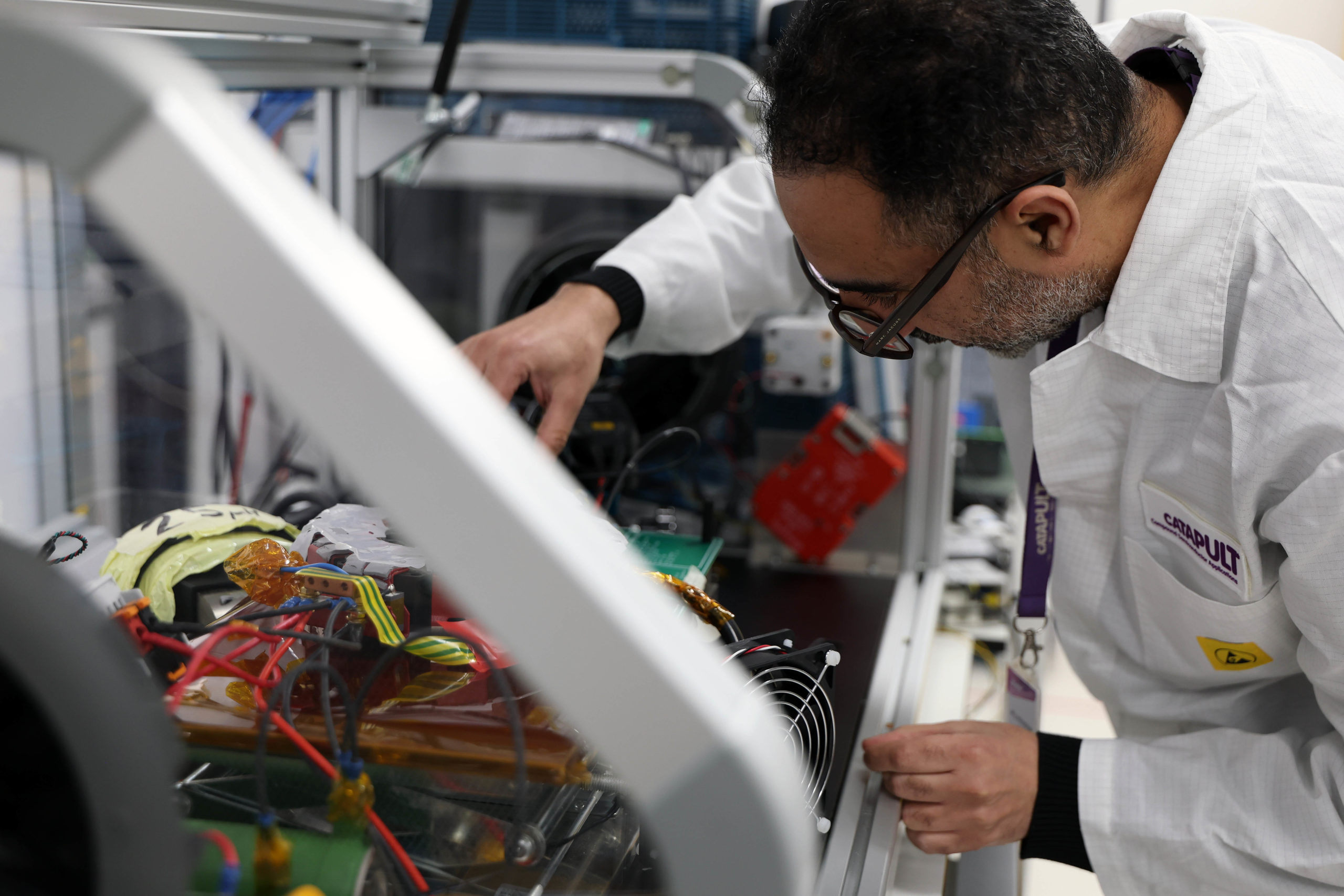 A man in a lab coat works on electronic components in a laboratory setting. - CSA Catapult