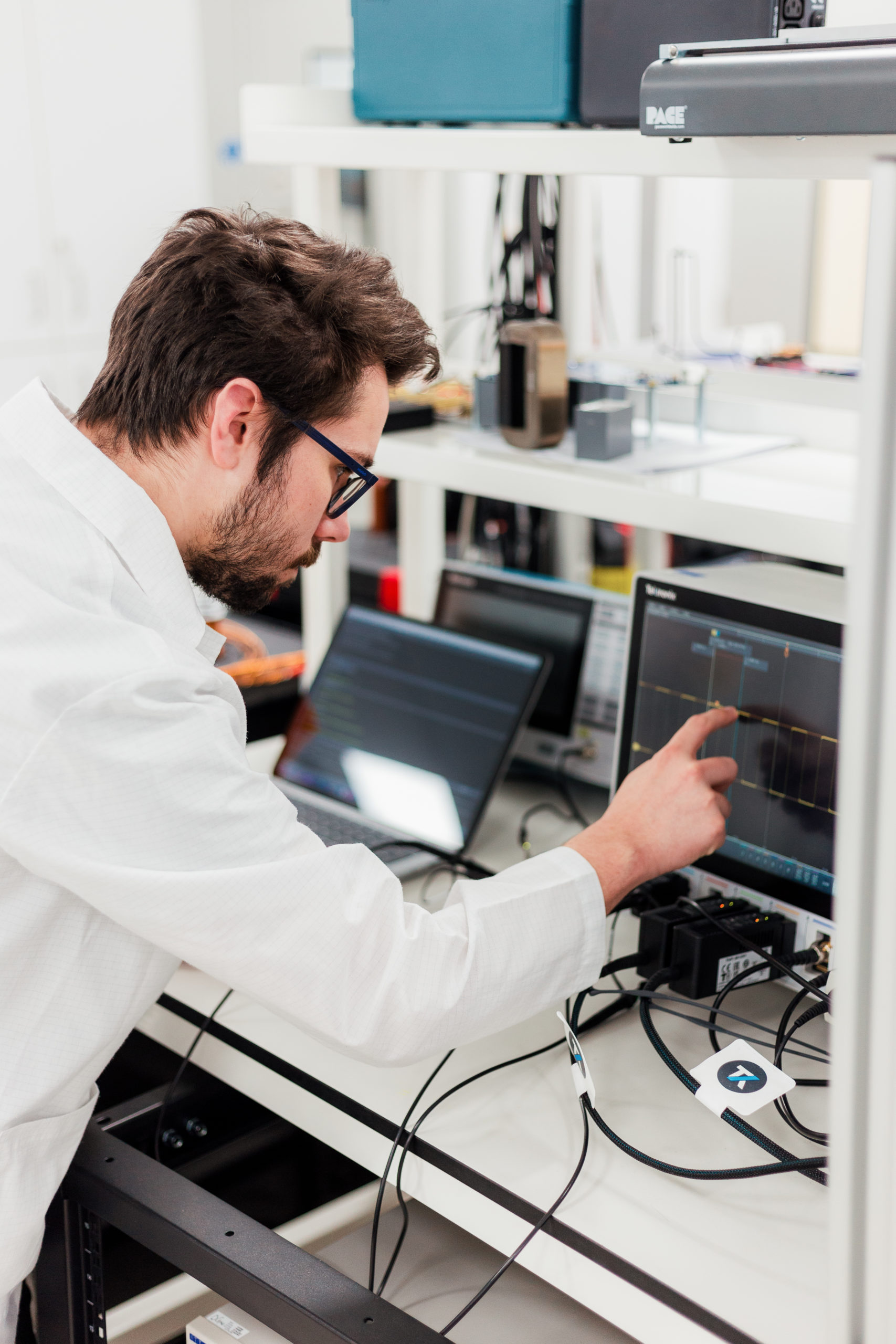A person in a lab coat analyses data on an oscilloscope in a laboratory setting. - CSA Catapult