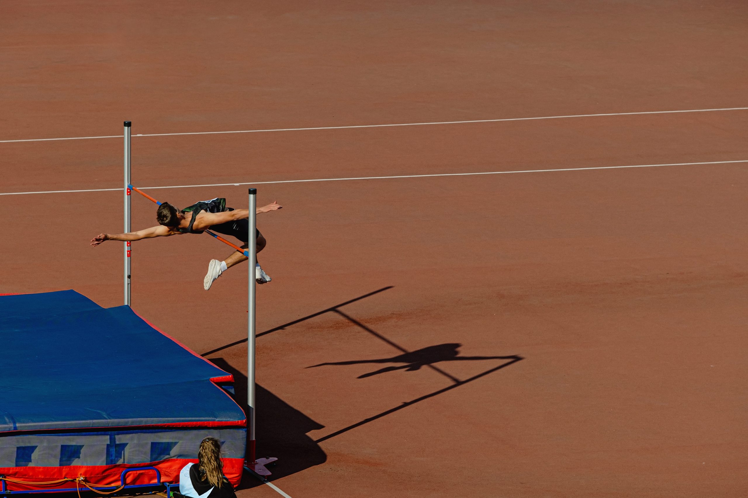 Athlete in mid-air attempting a high jump over a bar at an outdoor athletics event. - CSA Catapult