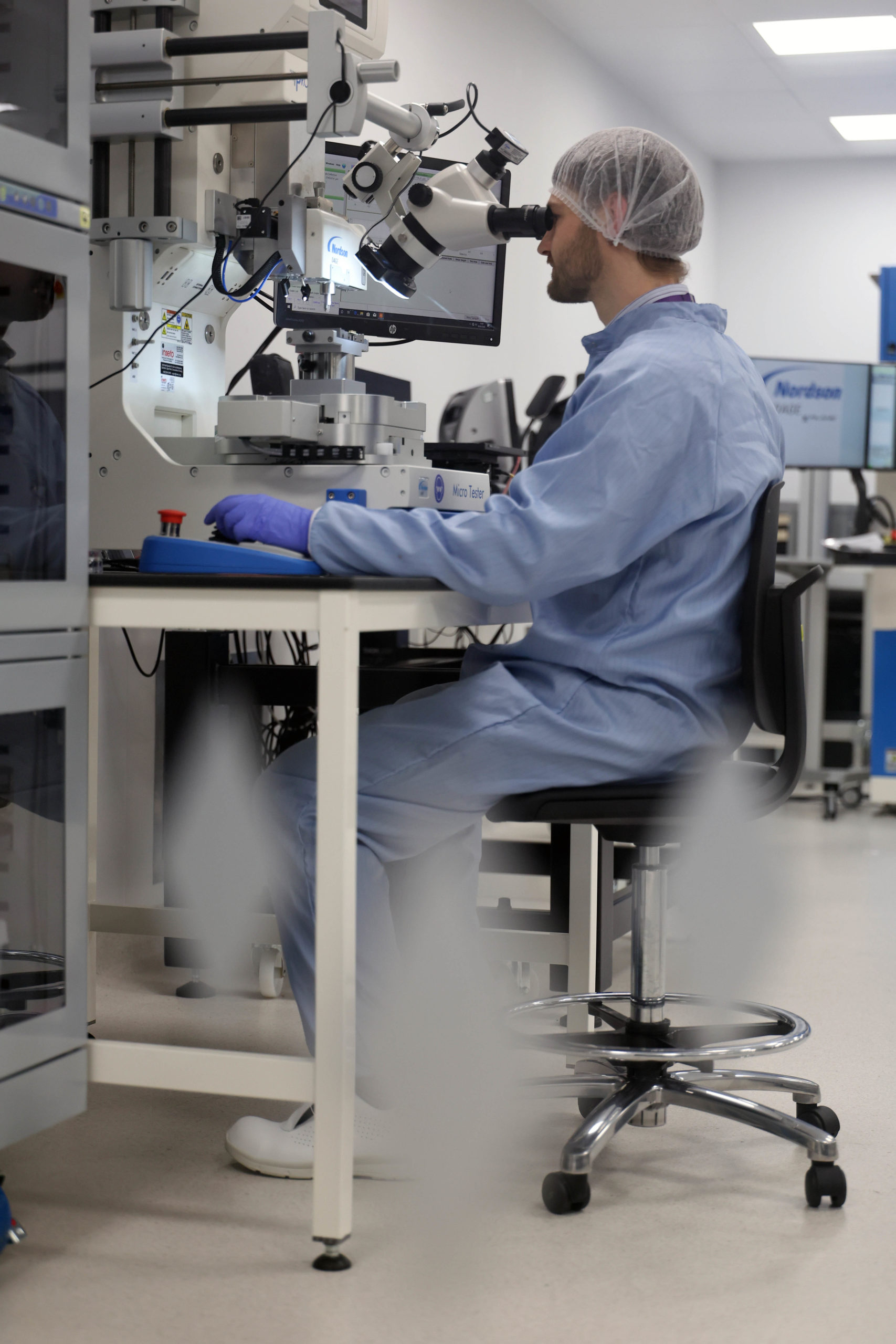 A scientist in protective gear uses AI technology while examining samples through a microscope in a laboratory. - CSA Catapult